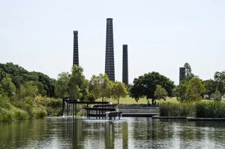Sydney Park wetlands with reflective water, native vegetation and the historic brick kiln chimneys rising above the landscape, showcasing the park's industrial heritage and environmental transformation.