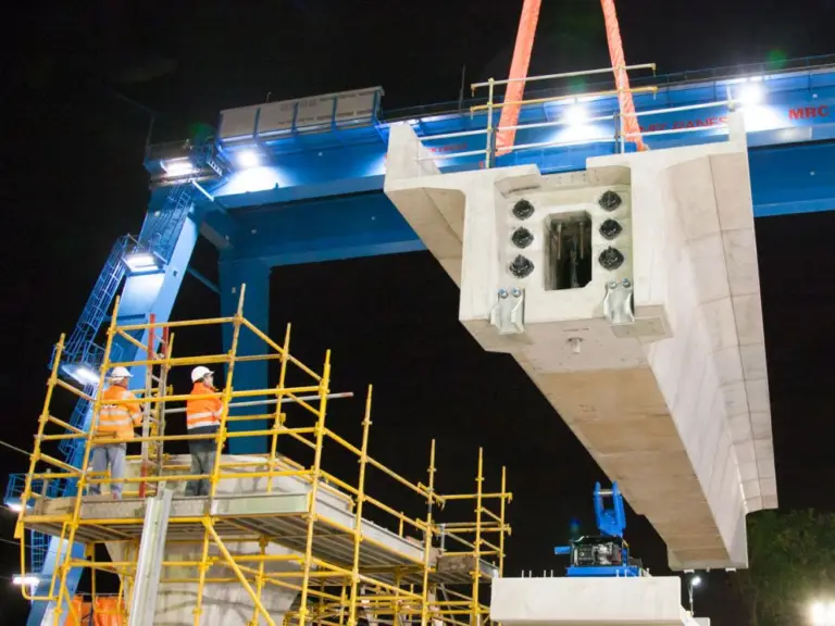 Straddle carrier lifting 600 tonne concrete rail span during Level Crossing Removal Project construction at night