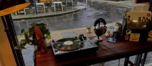 Record player playing vinyl beside headphones and coffee overlooking a rainy Ebenezer Place at Jewels of Thought Records in Adelaide's East End.
